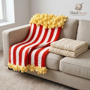 Puede incluir: Una manta caprichosa con temática de palomitas de maíz con rayas rojas y blancas, rematada con una textura amarilla similar a las palomitas de maíz. La manta está sobre un sofá beige, con dos mantas crema dobladas. El texto "Stitch Nexia" es visible.