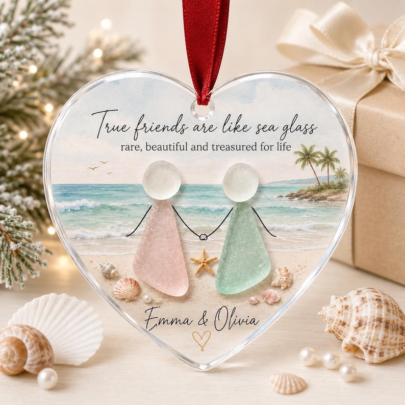 May include: A heart-shaped clear ornament featuring a beach scene with two figures made of sea glass, one pink and one light green. The text reads: True friends are like sea glass, rare, beautiful and treasured for life, Emma & Olivia.