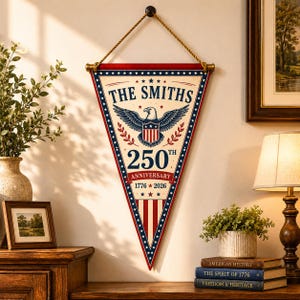 May include: A triangular wall pennant featuring a cream background with red and blue borders. It displays a bald eagle graphic, the text THE SMITHS, 250TH ANNIVERSARY, and 1776-2026. The pennant hangs from a wooden rod with a thick twisted rope cord.