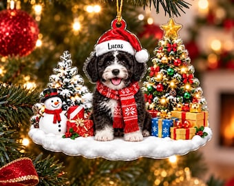 Könnte beinhalten: Ein flacher Acryl-Weihnachtsanhänger mit einem schwarz-weißen Welpen, der eine rote Weihnachtsmütze mit dem Namen Lucas auf dem Rand und einen roten gemusterten Schal trägt. Der Welpe sitzt auf einer verschneiten Basis mit Schneemann und Geschenken.