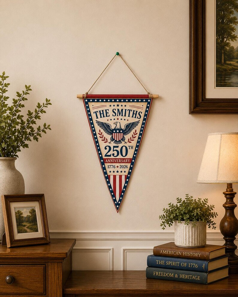 May include: A triangular wall pennant featuring a patriotic design with a central eagle emblem, the text THE SMITHS, 250TH ANNIVERSARY, and 1776-2026. The banner has a red, white, and blue color scheme with stars and stripes, suspended by a wooden rod.