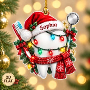 以下が含まれることがあります： 縁にSophiaという名前がプリントされた赤いサンタ帽をかぶった、歯の形の平らな吊り下げ式オーナメント。歯にはカラフルなクリスマスライトのストリング、白い雪の結晶模様が入った赤いニットのスカーフ、そして歯ブラシが巻き付けられています。