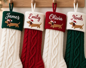 Può includere: Quattro calze natalizie in maglia appese a un supporto in legno. Ogni calza presenta un motivo a trecce, un risvolto a contrasto e un bassotto ricamato con cappello da Babbo Natale. I nomi James, Emily, Olivia e Noah sono ricamati sui risvolti.