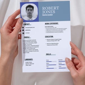 Puede incluir: Se muestra un currículum vitae de Robert Jones, diseñador gráfico. El documento incluye información de contacto, un perfil, experiencia laboral, educación, habilidades e idiomas. El diseño utiliza una combinación de colores azul y blanco.