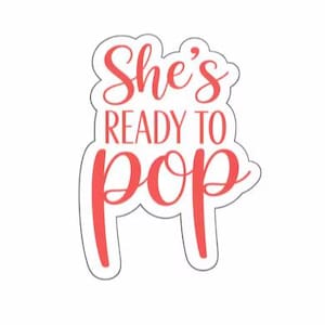 Könnte beinhalten: Ein Ausstechförmchen mit weißem Rand und korallenfarbenem Inneren, das den Text She's READY TO pop in einer Kombination aus Schreibschrift und serifenloser Schrift zeigt. Das Design folgt den Konturen der Buchstaben auf weißem Grund.