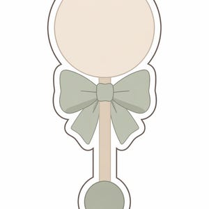 May include: A baby rattle cookie cutter in a simple, clean design. The rattle features a large circle at the top, a bow in the middle, and a smaller circle at the bottom. The color palette is soft, with a light green bow and a beige body.