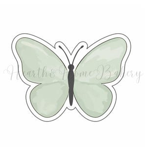 May include: A butterfly-shaped cookie cutter with a light green watercolor design. The cutter has a black outline and a black body. The wings are a soft, muted green. The image has the text "Hearth & Home Bakery" in a cursive font.