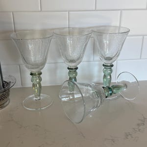 May include: Four clear glass goblets featuring a textured bubble finish on the bowl and a thick, sage green stem with a rounded, bulbous design. Three of the goblets stand upright on circular bases, while one goblet lies on its side.