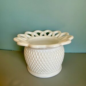 May include: A white milk glass bowl featuring a diamond-patterned texture on the exterior body and a wide, scalloped, lattice-style rim. The vessel has a rounded base and a smooth, glossy finish throughout its entire structure.