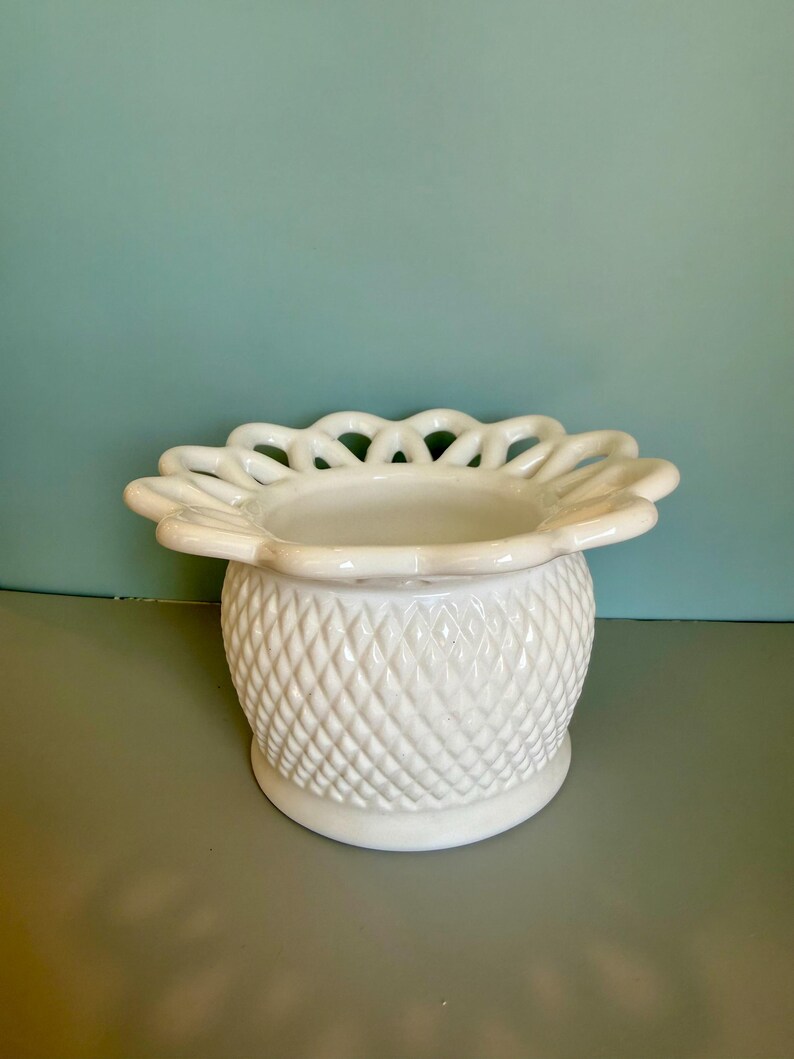 May include: A white milk glass bowl featuring a diamond-patterned texture on the exterior body and a wide, scalloped, lattice-style rim. The vessel has a rounded base and a smooth, glossy finish throughout its entire structure.