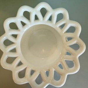 May include: A white milk glass bowl featuring a smooth, circular center basin surrounded by a wide, decorative lattice rim with a scalloped edge. The openwork design creates a repeating pattern of interconnected loops around the perimeter.