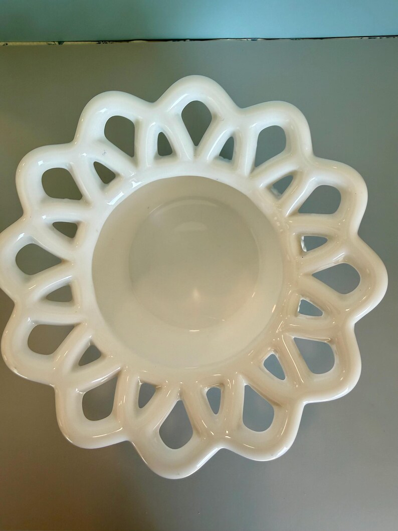 May include: A white milk glass bowl featuring a smooth, circular center basin surrounded by a wide, decorative lattice rim with a scalloped edge. The openwork design creates a repeating pattern of interconnected loops around the perimeter.