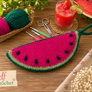 May include: A watermelon-shaped zippered pouch with black seed details, green rind, and a green loop handle. The pouch is on a wooden surface, alongside crochet supplies, a drink, and the text "pdf crochet".