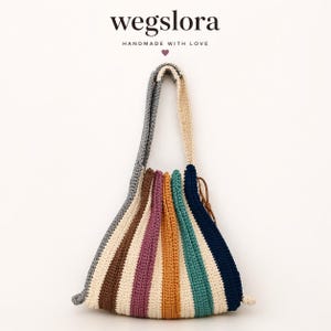 May include: A colourful, handmade crochet bag with a striped design in shades of grey, brown, purple, orange, teal, and navy. It features a drawstring closure and a long strap. The text "wegslora HANDMADE WITH LOVE" is visible at the top.