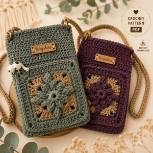 Könnte beinhalten: Zwei handgefertigte gehäkelte Handytaschen in Grün- und Lilatönen mit einem Blumendesign und einem gewebten Riemen. Jede Tasche hat ein kleines Lederetikett mit der Aufschrift "Wegslora". Die Taschen werden auf einer Holzoberfläche präsentiert.