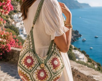 Puede incluir: Un bolso de hombro de ganchillo con un estampado floral en tonos rosa, amarillo y verde. El bolso tiene una correa verde y un cierre de botón de madera. El bolso se lleva al aire libre.