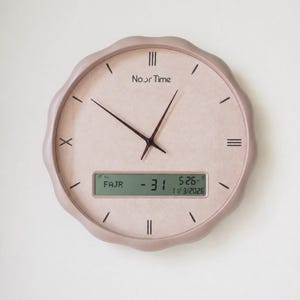 Peut inclure: Une horloge murale rose clair avec un cadran texturé et un bord ondulé. L'horloge a des aiguilles noires et des chiffres romains. L'écran numérique affiche "FAJR -31" et la date "5:26 11/3/2026". Le cadran de l'horloge indique "Noor Time".
