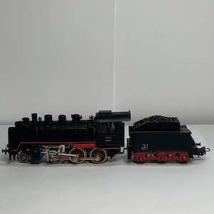 May include: A black model train with red and silver detailing. The train comprises a locomotive and a coal car. The wheels are red, and the model features intricate detailing. The model is set against a plain white background.