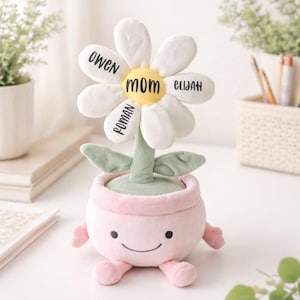 May include: A plush flower with white petals and a yellow center, labeled "MOM." The petals are inscribed with the names "OWEN," "ELIJAH," and "ROMAN." The flower sits in a pink pot with a smiling face and small arms and legs. Green leaves and stem.