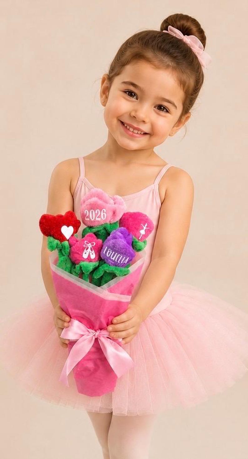 Op de afbeelding: Een jong meisje in een roze turnpakje en tutu houdt een boeket pluche bloemen vast. Het boeket bevat rode, roze en paarse bloemen met tekst en balletthema-ontwerpen. Het boeket is verpakt in roze papier en vastgebonden met een roze lint.