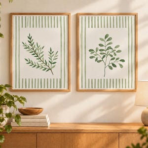 Puede incluir: Dos cuadros rectangulares con marcos de madera clara. Cada lámina presenta una ilustración botánica central de hojas verdes sobre fondo blanco, rodeada por un borde de rayas verticales verdes. La obra muestra un diseño limpio y sencillo.