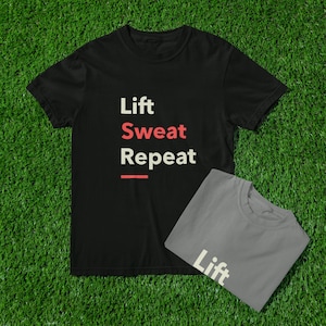Könnte beinhalten: Zwei T-Shirts auf einer grünen Oberfläche. Ein schwarzes T-Shirt mit den Worten "Lift Sweat Repeat" in Weiß und Rot. Ein graues T-Shirt mit dem Wort "Lift" in Weiß. Die Shirts sind wahrscheinlich für Fitness oder Training.