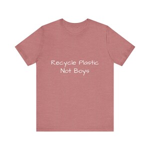 May include: A short-sleeved, dusty rose t-shirt with the white text "Recycle Plastic Not Boys" printed across the front. The shirt has a crew neck and a casual fit, suitable for everyday wear.