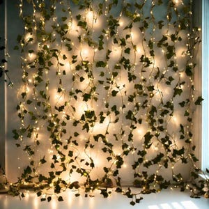 May include: A wall of artificial ivy vines with small, warm white LED lights. The green leaves are interspersed with the tiny lights, creating a soft, ambient glow. The vines hang vertically, suitable for home decor.
