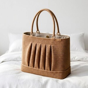 Op de afbeelding: Een gestructureerde, beige tas met een getextureerde, geweven buitenkant met vijf verticale plooien op het voorpaneel. De tas is voorzien van twee bijpassende handvatten, een lichtgekleurde voering, een goudkleurige drukknoopsluiting en een klein leren label met de tekst LYRA.