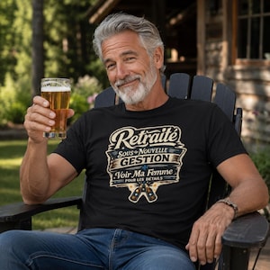 May include: A black t-shirt featuring a graphic with the text "Retraite SOUS NOUVELLE GESTION Voir Ma Femme POUR LES DÉTAILS" in white and beige lettering, accompanied by an illustration of two clinking beer bottles at the bottom.