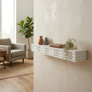 May include: A white floating shelf with a geometric design, holding decorative vases, a book, and a small plant in a gold geometric holder. The shelf is mounted on a light-colored wall, creating a modern, minimalist aesthetic.
