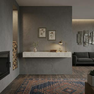 May include: A modern living room with a white floating shelf featuring a geometric design. The shelf holds a lamp, books, and decorative items. Two framed botanical prints hang above the shelf. A dark gray sofa and a patterned rug complete the space.