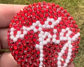 May include: A circular coaster decorated with a dense pattern of small, reflective red rhinestones. A white, stylized graphic of a moose is formed by a cluster of white beads embedded within the red rhinestone field, creating a high-contrast design.