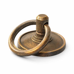 May include: A circular brass drawer pull featuring a weathered, antique finish. The hardware consists of a flat, round base plate with a central post and a hinged, movable ring handle that rests against the base. The metal surface shows texture.