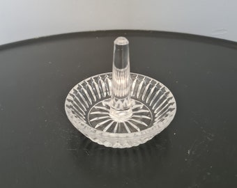 Op de afbeelding: Transparante glazen ringhouder met een centrale paal en een cirkelvormige basis. De basis heeft een geribbeld ontwerp en de paal is ontworpen om ringen vast te houden. De ringhouder is gemaakt van helder glas.