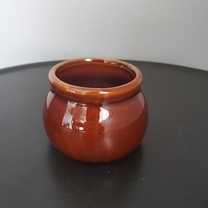 Puede incluir: Una pequeña maceta de cerámica marrón con forma redondeada y un acabado liso y brillante.