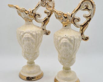 Könnte beinhalten: Zwei weiße Keramikvasen mit goldenen Akzenten und verzierten Designs. Die Vasen haben einen klassischen, eleganten Stil.