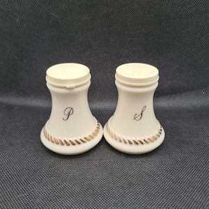 Puede incluir: Un juego de dos saleros y pimenteros de cerámica blanca con ribetes dorados. Los saleros están etiquetados con "P" y "S" para pimienta y sal.