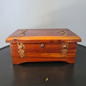 May include: A wooden box with a hinged lid and brass accents. The box is made of dark wood with a light wood trim. The box has a simple design with a rectangular shape and a flat lid.