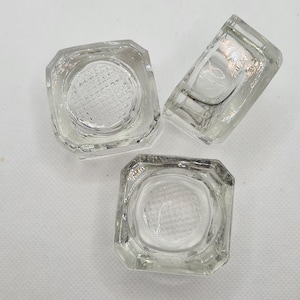 May include: Three clear glass square-shaped containers with a textured bottom.