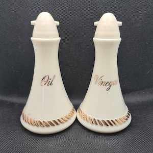 Puede incluir: Un juego de dos jarras de cerámica blanca para aceite y vinagre con ribetes dorados y las palabras "Aceite" y "Vinagre" escritas en ellas.