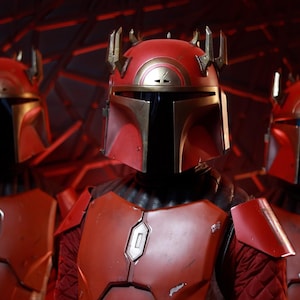 Puede incluir: Tres figuras con armadura mandaloriana roja y dorada se encuentran en un espacio con poca luz. Los cascos tienen un dise&ntilde;o distintivo con una visera en forma de T y una estructura similar a una corona. La armadura incluye petos y hombreras.