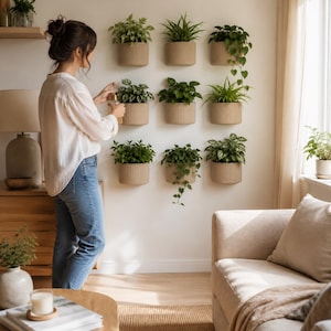 Può includere: Un set di nove vasi da parete cilindrici e scanalati di colore beige chiaro, disposti in una griglia tre per tre su una parete bianca. Ogni vaso contiene una diversa pianta verde da interno, con fogliame che ricade verso il basso.