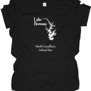 Pu&ograve; includere: T-shirt nera con grafica bianca del lago Norman, Carolina del Nord. La grafica include il contorno del lago e il testo "Lake Norman" sopra e "North Carolina's -Inland Sea-" sotto.