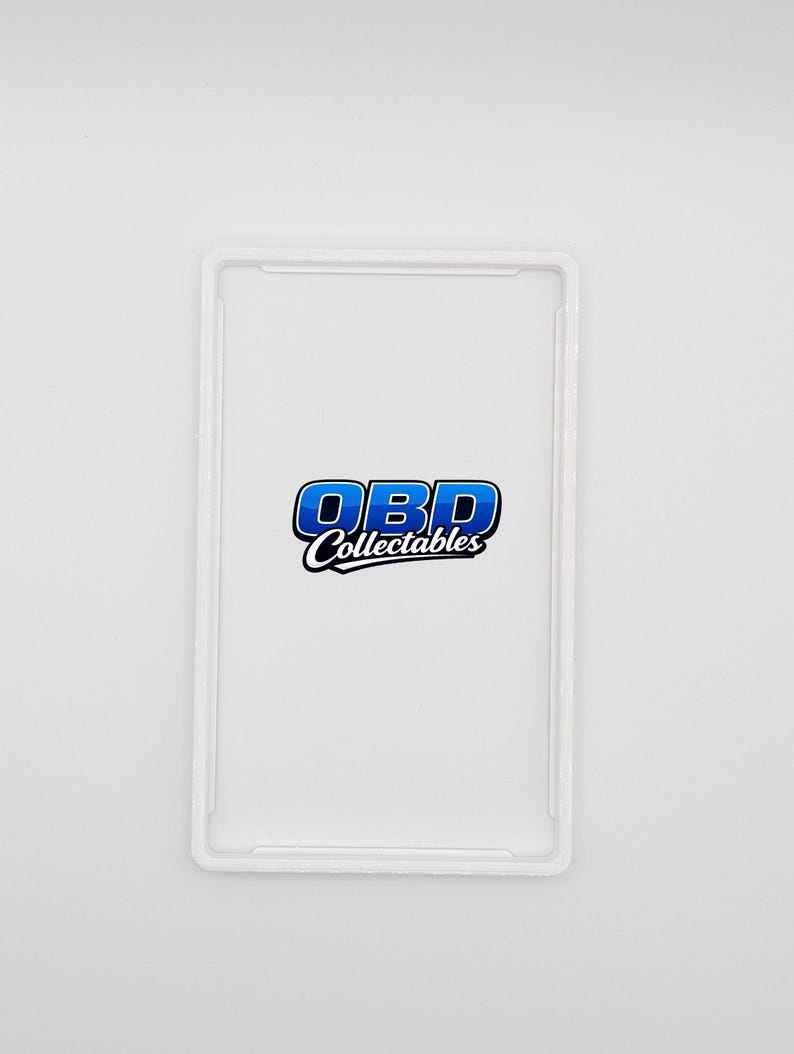 Pu&ograve; includere: Una custodia protettiva rettangolare trasparente con angoli arrotondati. La custodia presenta il testo "OBD Collectables" in blu e bianco, centrato sul davanti. La custodia &egrave; progettata per contenere un oggetto rettangolare.