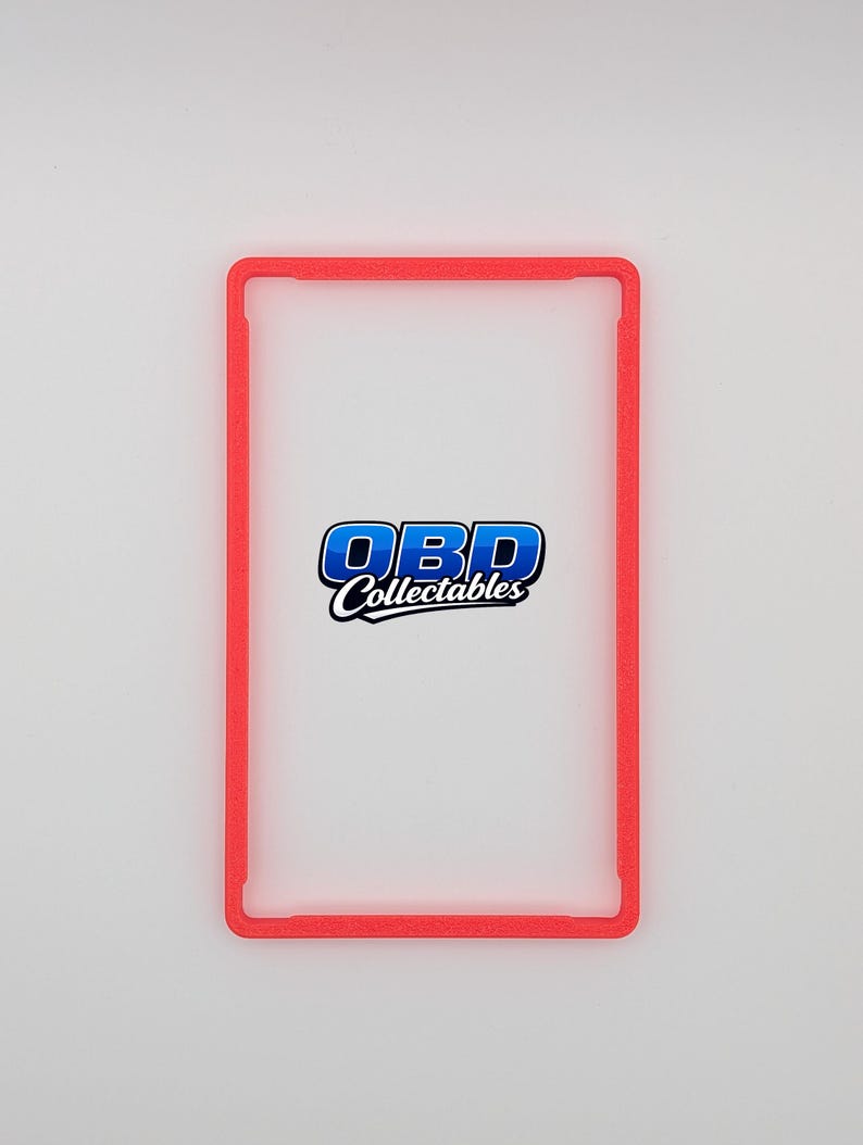 Pu&ograve; includere: Un porta carte rettangolare rosso con angoli arrotondati. Il supporto ha un centro trasparente e il testo "OBD Collectables" in blu e bianco. Il supporto &egrave; progettato per proteggere ed esporre carte collezionabili.