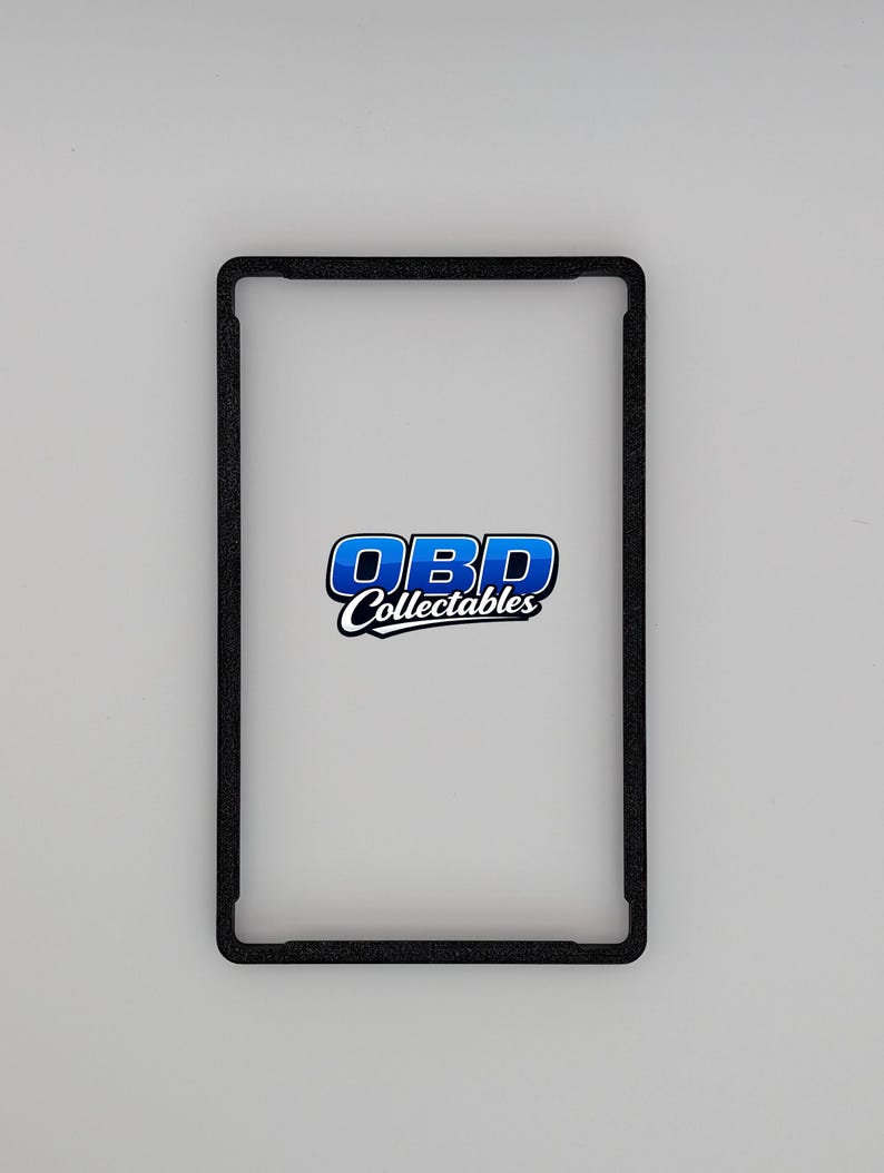 Pu&ograve; includere: Una cornice rettangolare nera con angoli arrotondati. La cornice circonda uno spazio bianco, con il testo blu e bianco "OBD Collectables" centrato all'interno. Lo sfondo &egrave; grigio chiaro.