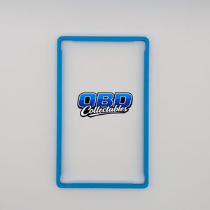 Pu&ograve; includere: Una cornice rettangolare blu chiaro con angoli arrotondati. La cornice circonda un interno bianco. Il testo "OBD Collectables" &egrave; visualizzato al centro della cornice in blu e bianco.