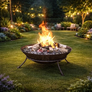 以下が含まれることがあります： 緑の芝生に置かれた、燃える火のある金属製のファイヤーピット。 ファイヤーピットには丸太が入れられ、小さな石で囲まれています。 背景には、木々とストリングライトのある庭があります。
