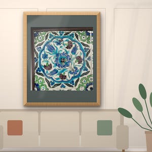 May include: A square ceramic tile featuring a central circular medallion with blue, green, and dark red floral motifs, including tulips and carnations, set within a light-colored border, displayed inside a simple wooden frame with a dark mat.